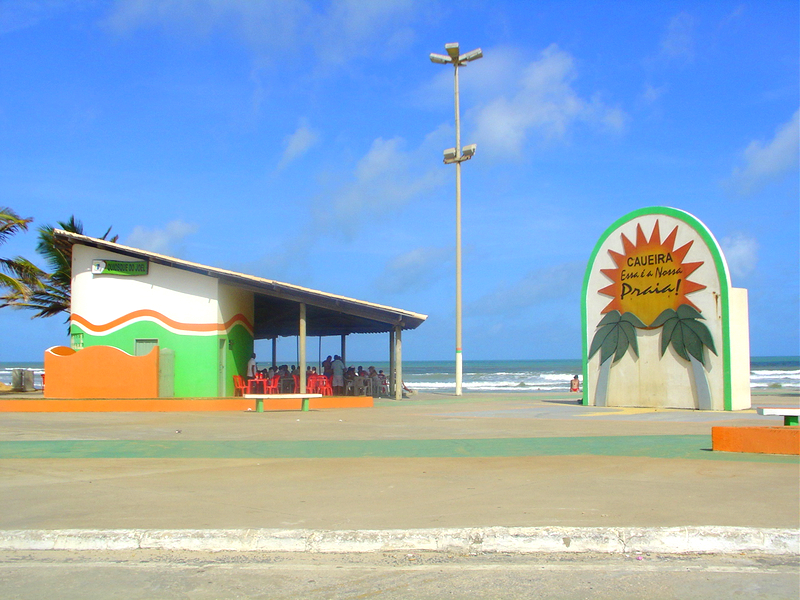 Registro da orla da Praia da Caueira, com letreiro de identificação e mar ao fundo